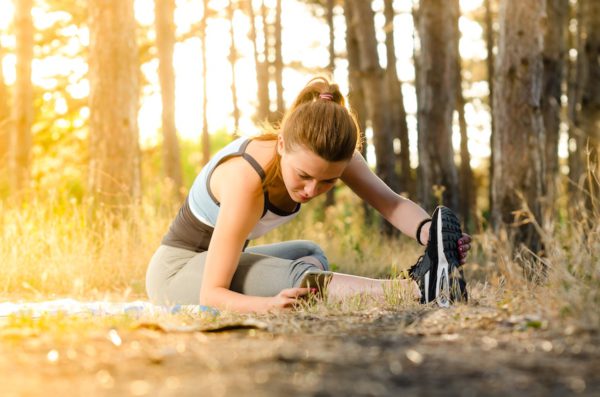 Mujer en ropa deportiva realizando estiramientos en el bosque con luz de atardecer para ilustrar concepto de rutinas para una vida más saludable