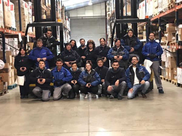 La plantilla de Cogesa se suma a FEDER por las enfermedades raras. Imagen de una de las centrales de logística de Cogesa en la que los trabajadores, con el uniforme corporativo, posan haciendo el gesto "red"